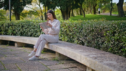 Focused girl reading book in sunlit park conveying peace. Woman enjoying leisure
