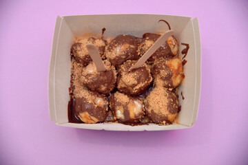Sweet donuts topped with cream and biscuits in a box. Photographed in the studio. Delicious and...