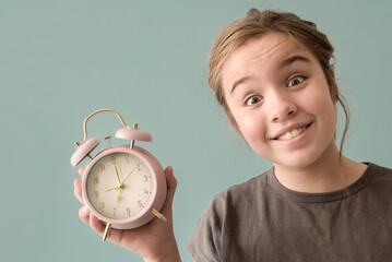 Smiling young girl holding a pink alarm clock on light green background
