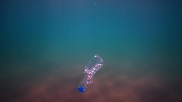 Plastic pollution, discarded plastic bottle drifting under the surface of the water in the sun's rays. plastic bottle in blue water.