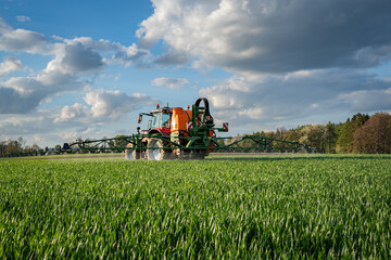 Getreideanbau - roter Traktor mit angebauter Feldspritze bei einer Pflanzenschutzmaßnahme im...