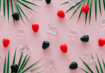 Creative summer pattern made of raspberries, blackberries, green tropical palm leaves and ice cubes...