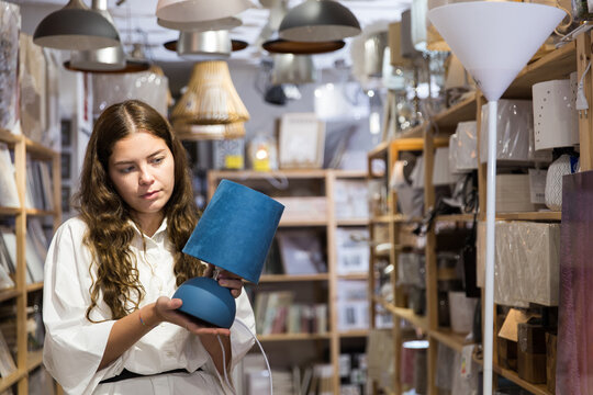Young woman buying table lamp at store of household goods