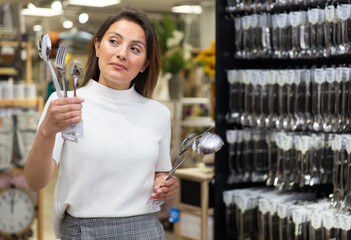 Portrait of young emotional female shopper looking for kitchen utensils at shop