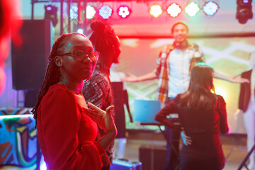 African american woman standing on dancefloor showing with hand at herself in nightclub. Young...