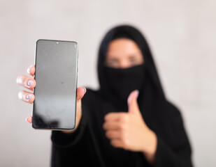 young Muslim girl with her face covered by burka hold in hand use close up mobile cell phone with...
