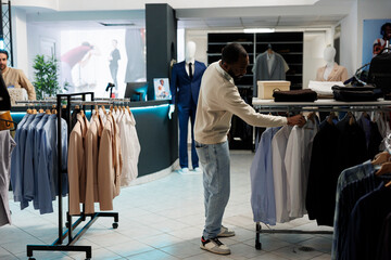 African american man searching shirt size while choosing formal wear outfit in clothing store....