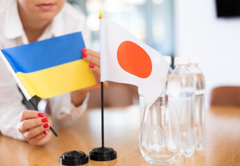 Closeup of table national flags of Ukraine and Japan in hands of female office manager preparing...