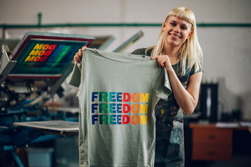 Happy print shop worker showing finished t-shirt at the camera,