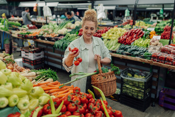 Smiling shopper woman with basket buying fresh vegetables at market.