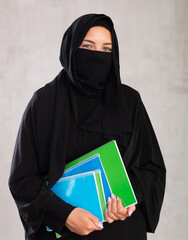 girl with face covered with burka holds lot of thick notebooks. foreign Muslim student with stack...