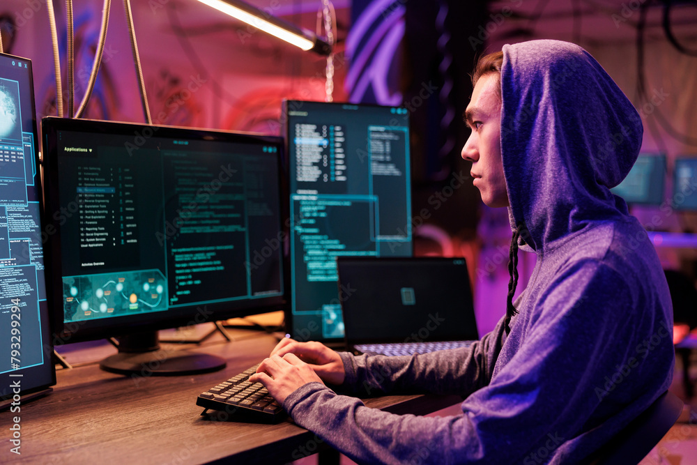 Poster asian hacker typing on keyboard and writing spyware code on computer. internet criminal in hood hack