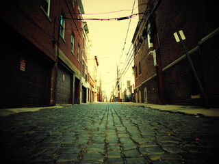 Quiet street scene of a narrow and empty cobblestone street lined with tall brick historic...