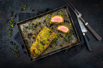 Fried mangalica pork tenderloin coated with crashed pistachio nuts, grated parmesan and chopped cranberries served with princess potatoes as top view on a rustic black metal tray with copy space