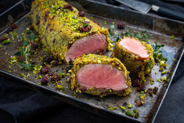 Fried mangalica pork tenderloin coated with crashed pistachio nuts, grated parmesan and chopped cranberries offered as close-up on a rustic black metal tray