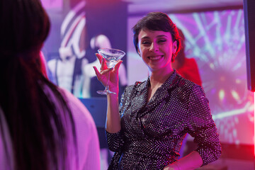 Smiling young woman drinking alcohol and partying on crowded nightclub dancefloor portrait....