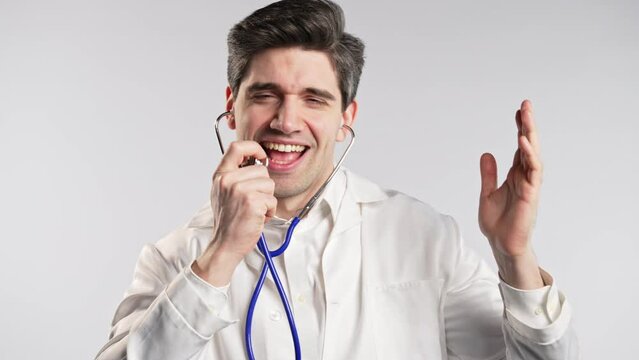 Smiling doctor funny dancing, singing to stethoscope, success and luck at work