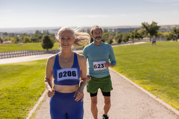 older friends run marathon in the park. Senior mature couple running together in competition in the park while the woman wins in the front line