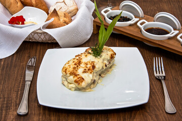 Fish dish with melted cheese accompanied by sauce and glass of white wine on restaurant table