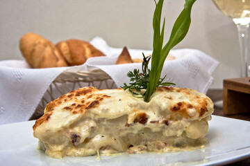 Fish dish with melted cheese accompanied by sauce and glass of white wine on restaurant table