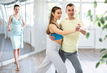 Confident couple, woman and man in activewear rehearsing elegant tango in pair, participating in...
