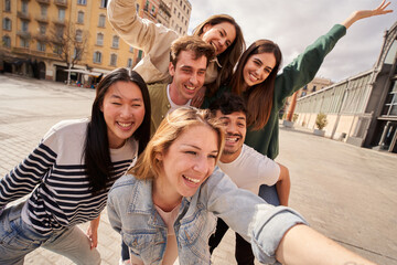 A group of young people is happily posing for a selfie together while traveling. They are smiling and making gestures of fun and leisure under the clear sky, sharing a moment of recreation and joy