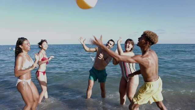 Young group of friends having fun playing with beach ball in to water during summer vacation