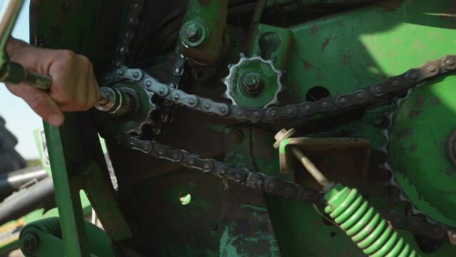 Close shot of a man working on the gears of a broken farm tractor