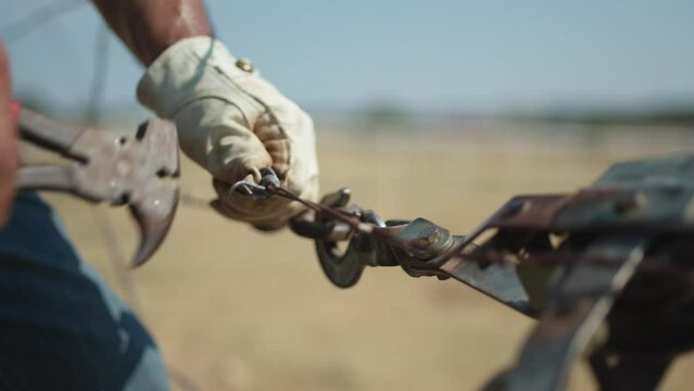 Tight shot of a rancher fixing a barbed wire fence with gloves and tools