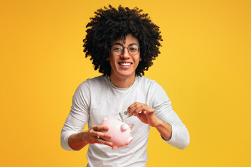Smiling african-american man putting money in his piggy bank