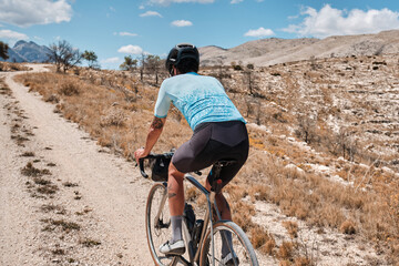 Cyclist riding gravel bike on gravel road in mountains with scenic view. Cyclist practicing on gravel road. Man cyclist wearing cycling kit and helmet. Alicante region in Spain.