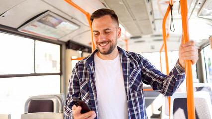 Young man riding in a bus and sending message on smartphone