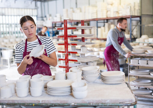 Interested professional young female ceramicist closely examining batch of slipcast pottery, inspecting technique and quality of workmanship in ceramic workshop.. - Powered by Adobe