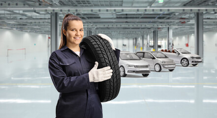 Young female mechanic worker carrying a car tire in a garage