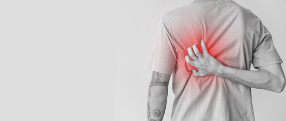 Young man suffering from back pain on light background, closeup