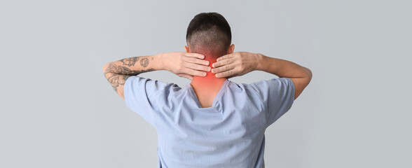 Young man suffering from neck pain on light background, back view