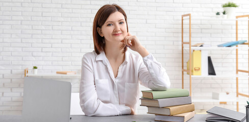 Young businesswoman with modern laptop and books at table in office