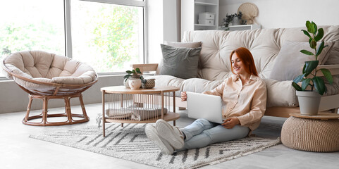 Young woman with laptop sitting on carpet in living room