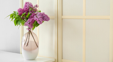 Vase with lilac flowers on table near folding screen
