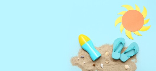 Bottle of sunscreen cream, flip-flops, paper sun and sand on light blue background with space for...