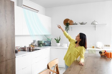 Asian woman switching on air conditioner in kitchen