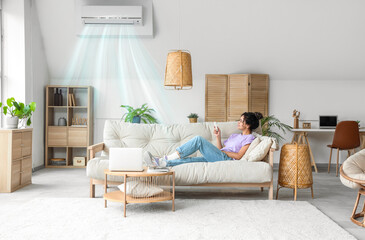 Young woman switching on air conditioner at home