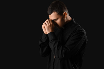 Young priest praying on dark background