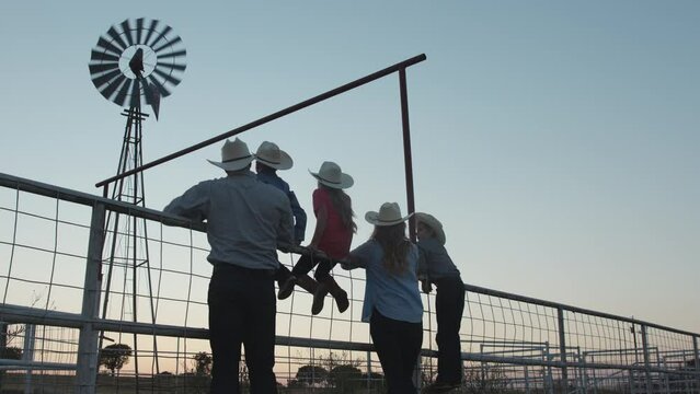 A family of five watches the sunset as the sit on a pasture gate