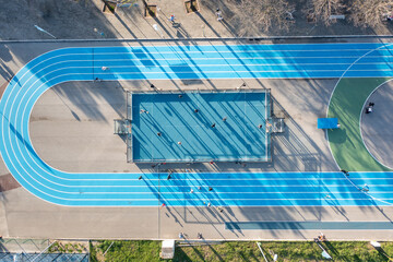 Aerial view of blue running track and multi-sport court in public park. Used to practice football, basketball jogging. Top view. Sunny day. Sunset. Drone photo.