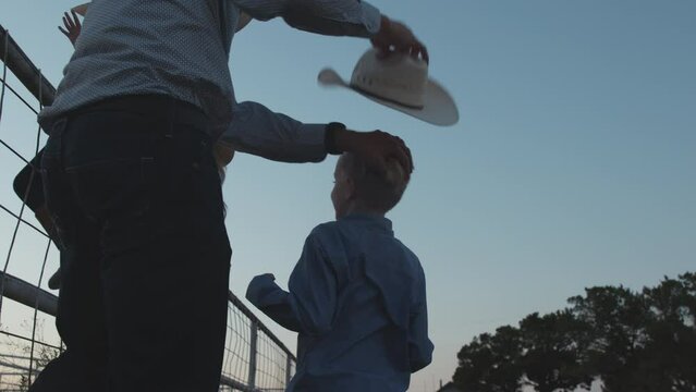 A dad lifts his son to sit on the pasture gate to watch the sunset with his siblings