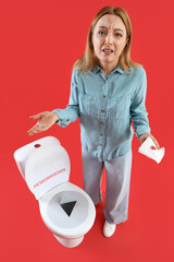 Mature woman with bloody paper and thumbtack on toilet bowl against red background. Hemorrhoids...