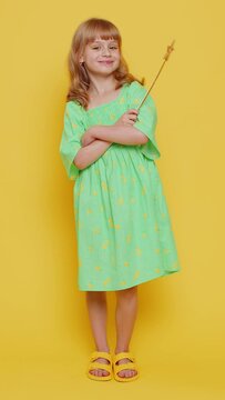 Magician school girl witch gesturing with magic wand fairy stick, making wish come true, casting magician spell, advertising holiday sale discount. Child kid isolated on yellow background. Vertical