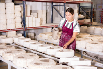 Focused diligent young female ceramicist engaged in creating ceramics in sunlit workshop, pouring...