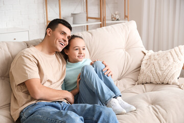 Happy father with his little daughter watching TV on sofa at home